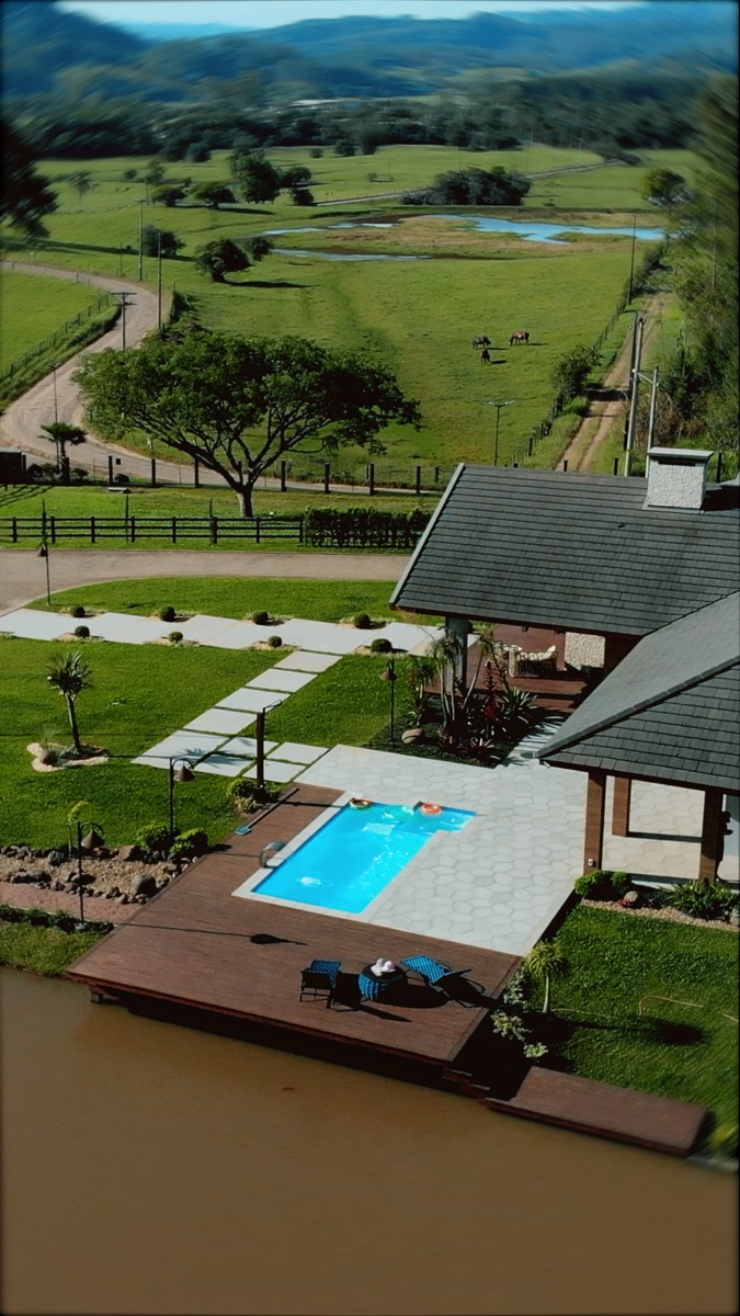 Vista aérea de uma piscina Fyber Show instalada ao lado de uma casa de campo, com o vale ao fundo